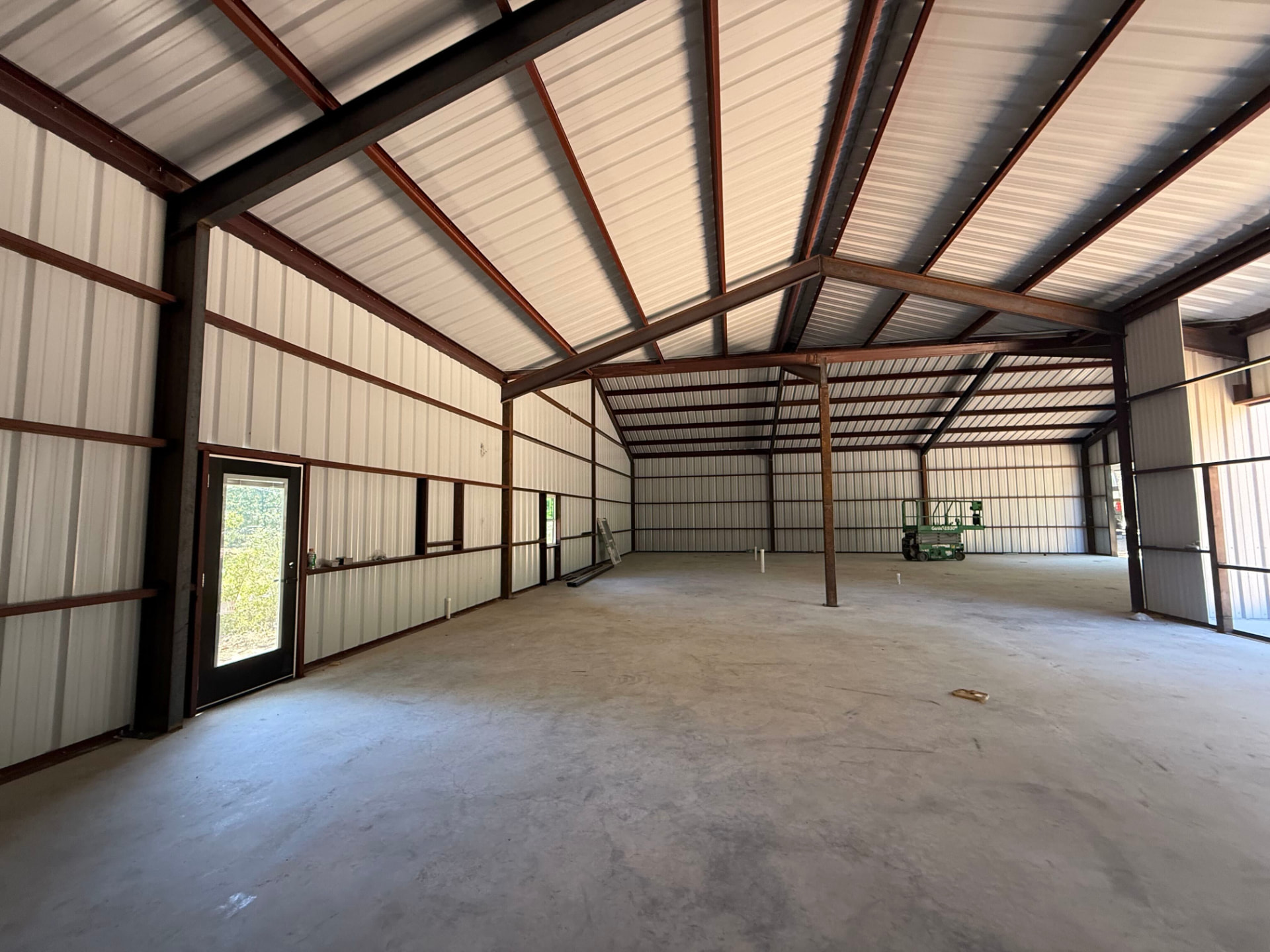 Open interior of a red iron metal building with white wall panels, exposed rafters, and a concrete slab floor