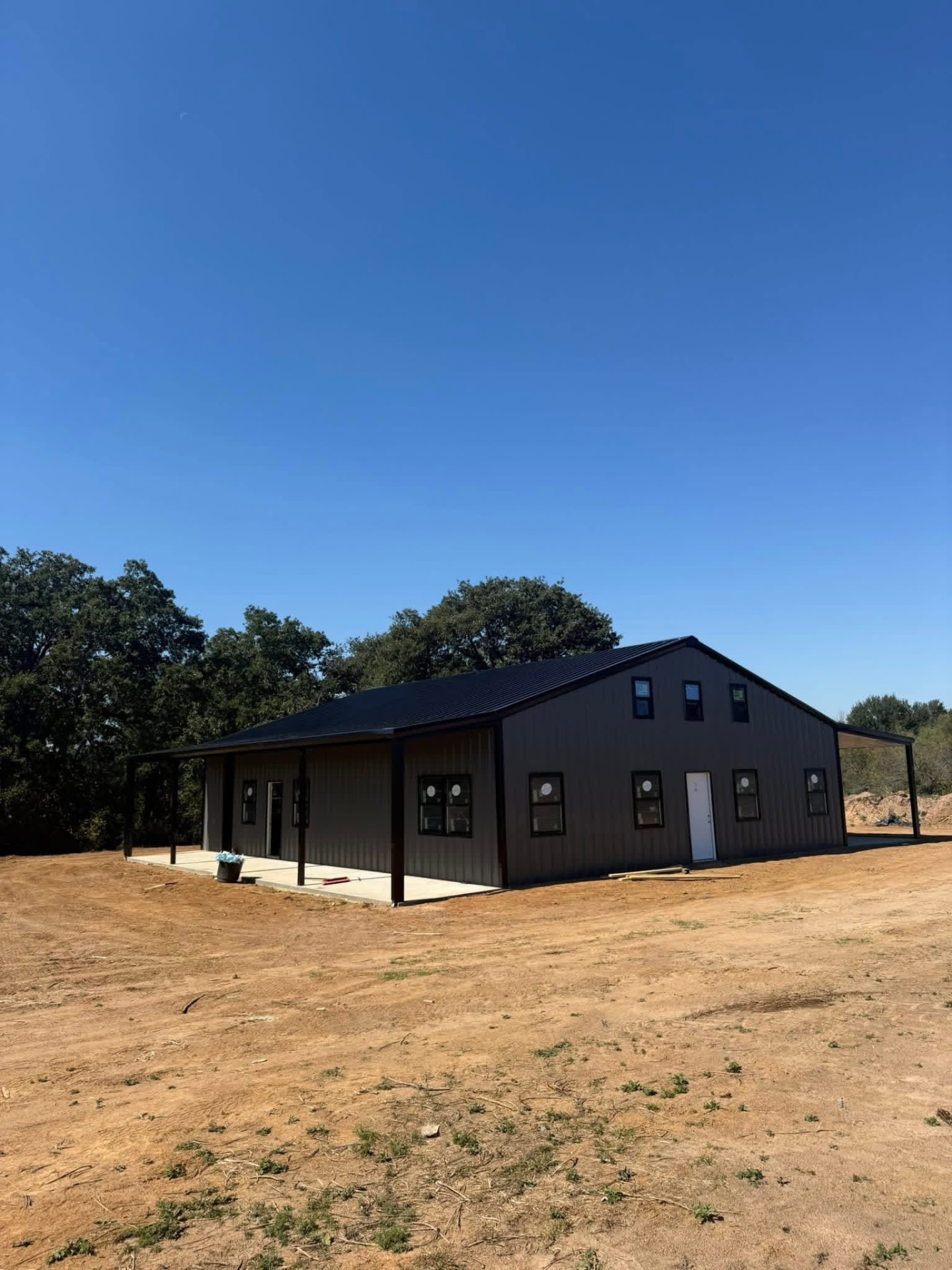 Gray metal home with a dark metal roof, covered porch, dormer windows, and side porches on a clear day